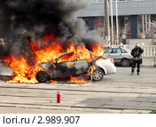 Пожарный стоит возле горящего легкового автомобиля (2010 год). Редакционное фото, фотограф Егор Никифоров / Фотобанк Лори