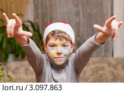 Весёлый мальчик в шапке Санта Клауса с разрисованным лицом поднял руки вверх. Стоковое фото, фотограф Игорь Низов / Фотобанк Лори