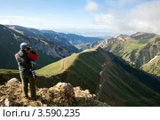 Турист фотографирует вид на ущелье с извилистой дорогой в горах Тянь-Шаня. Стоковое фото, фотограф Николай Винокуров / Фотобанк Лори