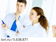 Концепция взаимодействия. Коллеги стоят у флипчарта.  Улыбающаяся девушка пишет синим маркером, мужчина в галстуке стоит рядом. Стоковое фото, фотограф Sergey Nivens / Фотобанк Лори