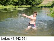 Полный десятилетний мальчик брызгается водой, стоя в реке. Стоковое фото, фотограф Володина Ольга / Фотобанк Лори