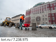 Работник ЖКХ разбрасывает противоледный реагент на тротуаре Тверской улицы напротив реконструируемого здания Моссовета (2013 год). Редакционное фото, фотограф Сайганов Александр / Фотобанк Лори
