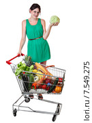 Shopping trolley filled food, young woman is holding a cabbage. Девушка в зеленом платье, возраст 19 лет,  стоит возле переполненной продуктовой тележки из универсама, улыбается, держит в руке кочан капусты, изолировано на белом фоне, сохранен путь выделения. Стоковое фото, фотограф Владимир Григорьев / Фотобанк Лори