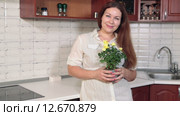 Довольная женщина с цветочным горшком и цветами стоит на кухне и смотрит в камеру. Стоковое видео, видеограф Кекяляйнен Андрей / Фотобанк Лори