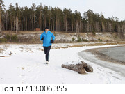 Мужчина в синей куртке бежит по снегу на берегу реки. Стоковое фото, фотограф Наталия Макарова / Фотобанк Лори