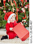 Little girl dressed in santa suit sits under Christmas tree on furry rug, holding red gift box. Стоковое фото, фотограф Losevsky Pavel / Фотобанк Лори