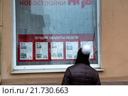 Девушка в шапке смотрит предложения по продаже недвижимости в витрине агентства недвижимости в центре города Москвы, Россия (2016 год). Редакционное фото, фотограф Николай Винокуров / Фотобанк Лори
