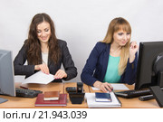 Две молодые девушки работают в офисе, одна весело взяла лист бумаги, вторая смотрит в экран компьютера. Стоковое фото, фотограф Иванов Алексей / Фотобанк Лори