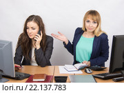 Девушка в офисе недоуменно указывает на коллегу, разговаривающую по телефону. Стоковое фото, фотограф Иванов Алексей / Фотобанк Лори