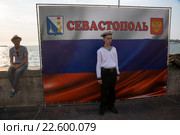 Молодые люди на набережной города Севастополя стоят у плаката с российским триколором, Республика Крым (2015 год). Редакционное фото, фотограф Николай Винокуров / Фотобанк Лори