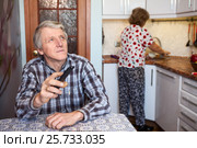 Жена моет посуду в раковине, муж смотрит телевизор за столом на кухне (2016 год). Редакционное фото, фотограф Кекяляйнен Андрей / Фотобанк Лори