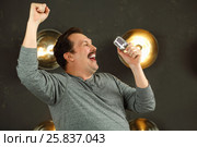 Smiling man with mustache sings with microphone in studio with lamps on wall. Стоковое фото, фотограф Losevsky Pavel / Фотобанк Лори