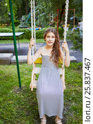 Girl sits on swings on a sunny day in green park. Стоковое фото, фотограф Losevsky Pavel / Фотобанк Лори