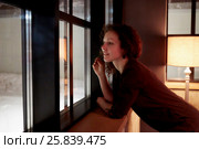 Young curly woman looks in window leaning her elbows on windowsill in room with torchiere. Стоковое фото, фотограф Losevsky Pavel / Фотобанк Лори