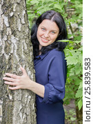 Portrait of smiling dark-haired woman peeking out from behind the tree in green summer park. Стоковое фото, фотограф Losevsky Pavel / Фотобанк Лори