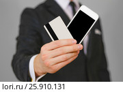 Businessman showing closeup of white smartphone with blank black screen and a credit card. Phone and card hold hands. Show clear telephone. Man in a black suit, white shirt and tie. Стоковое фото, фотограф Плотников Дмитрий / Фотобанк Лори
