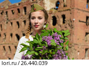 A young girl in a second world war epoch head-dress holding a lilac bouquet against the demolished building background. Стоковое фото, фотограф Макалиш Андрей / Фотобанк Лори