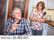 Строгая жена с поварешкой стоит позади мужа, смотрящего телевизор на кухне. Стоковое фото, фотограф Кекяляйнен Андрей / Фотобанк Лори