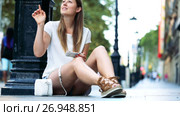 Smiling girl standing outdoors near lamp post using phone to find right address. Стоковое видео, видеограф Яков Филимонов / Фотобанк Лори