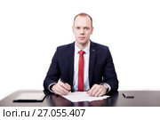 Portrait of confident young realtor in suit sitting at desk, signing contract, looking straight at desk, tablet, phone, on white background. Стоковое фото, фотограф Артём Зайцев / Фотобанк Лори