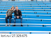 Young couple sitting on empty stadium sector on competition. Woman pointing and explaining the man with arms. Стоковое фото, фотограф Кекяляйнен Андрей / Фотобанк Лори