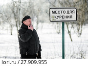Мужчина курит сигарету возле таблички "Место для курения" зимой. Стоковое фото, фотограф Игорь Низов / Фотобанк Лори
