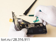 Руки в белых перчатках с помощью отвертки разбирают смартфон для ремонта. Стоковое фото, фотограф Наталья Гармашева / Фотобанк Лори