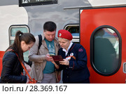 Проводница сверяет паспортные данные и билеты пассажиров на перроне около вагона поезда (2018 год). Редакционное фото, фотограф Дмитрий Рыженков / Фотобанк Лори