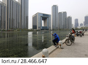 TIANJIN, CHINA - APRIL 8, 2017. A modern building along the Haihe River and fishermen in Tianjin, China. Редакционное фото, фотограф Яна Королёва / Фотобанк Лори