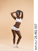 Full-length portrait of a sporty young cheerful african woman standing on beige background. Стоковое фото, агентство Ingram Publishing / Фотобанк Лори