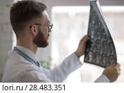 Closeup portrait of intellectual man healthcare personnel with white labcoat, looking at brain x-ray radiographic image, ct scan, mri, clinic office background. Radiology department. Стоковое фото, агентство Ingram Publishing / Фотобанк Лори