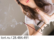 Young woman sitting in meditation pose in front of tea set and aroma sticks. Relaxation concept. Стоковое фото, фотограф Kirill Kedrinskiy / Ingram Publishing / Фотобанк Лори
