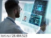 Closeup portrait of intellectual man healthcare personnel with white labcoat, looking at brain x-ray radiographic image, ct scan, mri, clinic office background. Radiology department. Стоковое фото, агентство Ingram Publishing / Фотобанк Лори