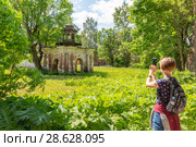 Туристка фотографирует колодец-голубятню усадьбы графа С.А.Строганова (18-19 века). Псковская область, Порховский район, пос.Волышово (2018 год). Редакционное фото, фотограф Сергей Васильев / Фотобанк Лори