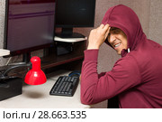 Интернет тролль у компьютера. Агрессивный молодой человек ехидно улыбается, занимаясь троллингом в сети. Стоковое фото, фотограф Лариса Капусткина / Фотобанк Лори