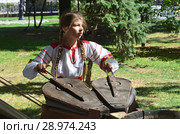 Москва, молодая девушка в народном платье раздувает меха старинной кузнечной печи на Чистопрудном бульваре в период проведения фестиваля "Времена и эпохи" (2018 год). Редакционное фото, фотограф Овчинникова Ирина / Фотобанк Лори
