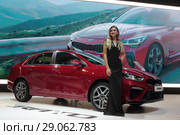 Московский автосалон 2018 года, девушка модель у красного автомобиля KIA на фоне рекламного видеоролика. Редакционное фото, фотограф Дмитрий Неумоин / Фотобанк Лори