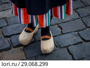 Девушка в традиционной голландской одежде и деревянных башмаках (кломпах) стоит на булыжной мостовой в центре европейского города (2018 год). Стоковое фото, фотограф Николай Винокуров / Фотобанк Лори