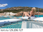 Woman relaxing on a summer sailing cruise, sitting on a luxury catamaran near picture perfect white sandy beach on Spargi island in Maddalena Archipelago, Sardinia, Italy. Стоковое фото, фотограф Matej Kastelic / Фотобанк Лори