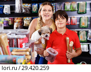 Cheerful woman with preteen son buying dog treats and chews in store to reward their precious pup. Стоковое фото, фотограф Яков Филимонов / Фотобанк Лори