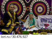 Мужчина и девочка в национальных костюмах сидят за праздничным дастарханом на стенде Республики Таджикистан на фестивале "Московский Навруз" в выставочном комплексе ВДНХ в городе Москве, Россия (2019 год). Редакционное фото, фотограф Николай Винокуров / Фотобанк Лори