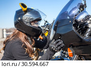 Biker girl in helmet looking in headlight of her bike and touching plastic front cowl. Стоковое фото, фотограф Кекяляйнен Андрей / Фотобанк Лори