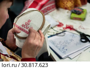 Мастерица вышивает национальный русский узор красной нитью на белой льняной салфетке (2015 год). Редакционное фото, фотограф Светлана Васильева / Фотобанк Лори