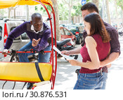 Driver of pedicab offering tour to couple. Стоковое фото, фотограф Яков Филимонов / Фотобанк Лори