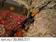 Автомат Калашникова лежит на ковре на площадке реконструкции лагеря афганцев во время войны советских войск в Афганистане, фестиваль "Времена и эпохи" в Москве (2019 год). Редакционное фото, фотограф Николай Винокуров / Фотобанк Лори