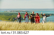 People in traditional russian clothes walking on the field and singing a song - a man holding balalaika. Стоковое видео, видеограф Константин Шишкин / Фотобанк Лори
