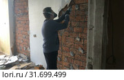 Construction repair in the apartment. The young man a manual construction instrumet removes a hundred-swarm a covering from a red brick wall. Стоковое видео, видеограф Куликов Константин / Фотобанк Лори