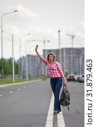 Hitchhiker waving hands for car stop, attractive mature woman with backpack standing on roadside. Стоковое фото, фотограф Кекяляйнен Андрей / Фотобанк Лори