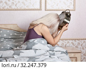 Расстроенная женщина, повесив голову, сидит с будильником в спальной комнате. Проспала. Стоковое фото, фотограф Элина Гаревская / Фотобанк Лори