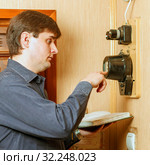 The man takes the readings of the apartment electric meter and writes it in the notebook. Стоковое фото, фотограф Акиньшин Владимир / Фотобанк Лори